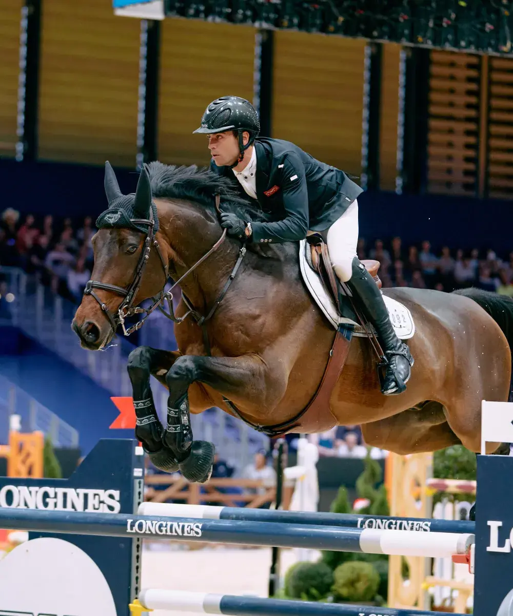 Cavalier en plein saut d’obstacle lors d’une compétition au Salon du Cheval de Paris, capturé depuis l’espace VIP pour une expérience immersive et exclusive.