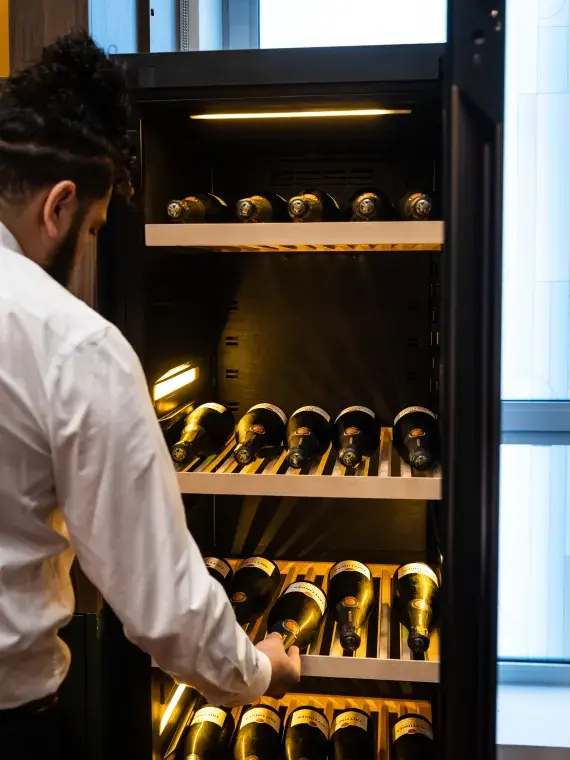 Staff member retrieving a bottle of champagne from a dedicated fridge where several bottles are neatly stored.