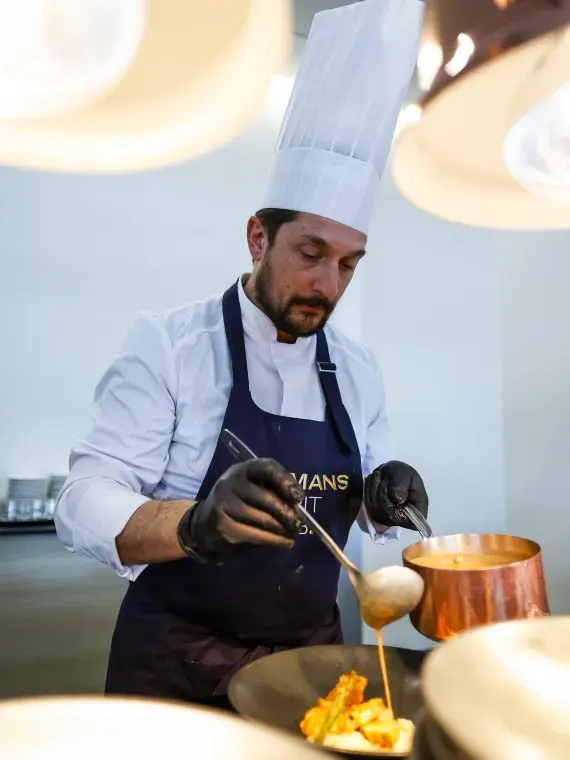 Un chef prépare un plat avec précision et créativité, mettant en lumière l’excellence culinaire de Sodexo Live! Hospitality lors des événements.