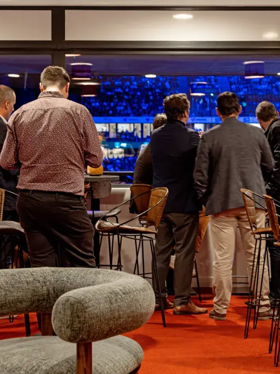 Inside the Club des Légendes, with guests watching the start of the match through the glass windows while enjoying a drink.