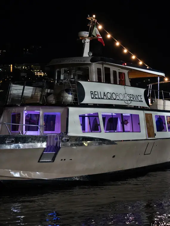 Boat sailing on Lake Como, surrounded by mountains, illustrating the cruise included in Sodexo Live! Hospitality’s VIP offers.