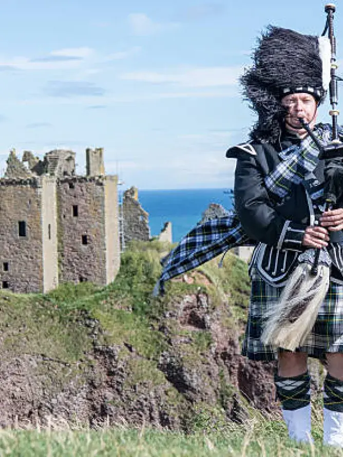 Joueur de cornemuse écossais en tenue traditionnelle jouant sur le Royal Mile à Édimbourg, devant un chateau et la mer