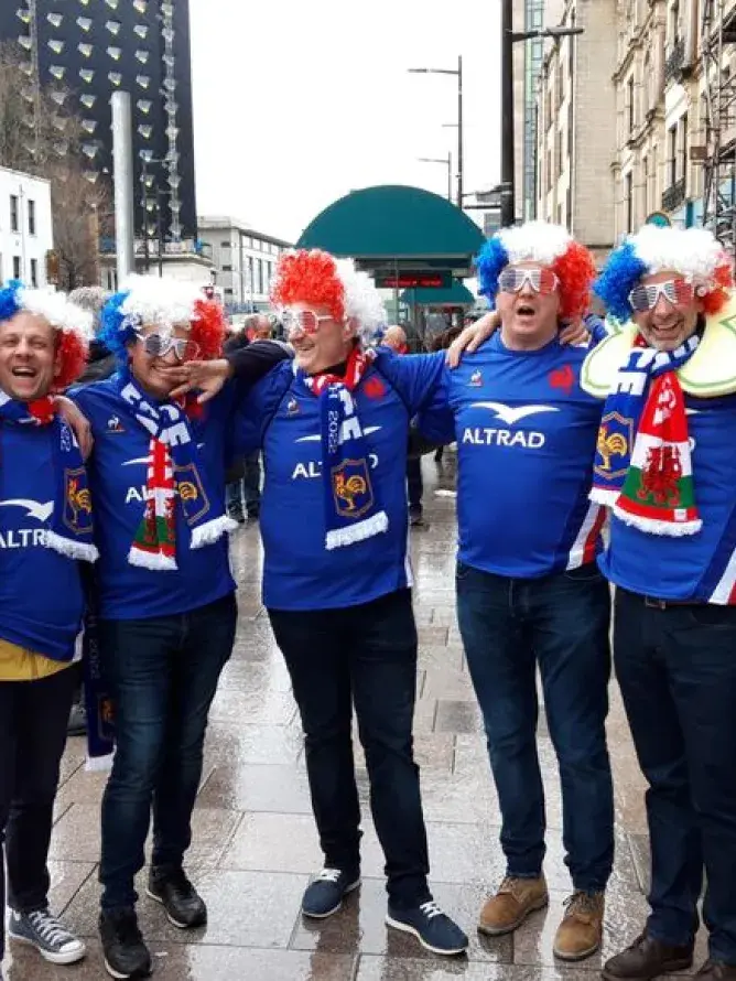 Supporters français en maillot bleu, drapeaux tricolores à la main, chantant dans les rues animées de Cardiff avant le match du Tournoi des 6 Nations
