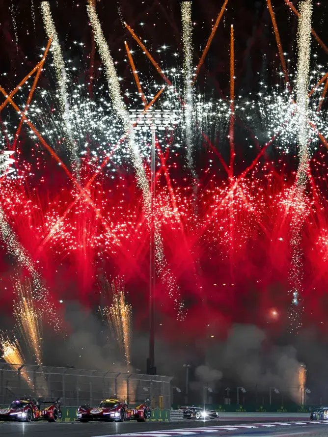 A race car reaches the finish at the World Endurance Championship as fireworks explode in the background.