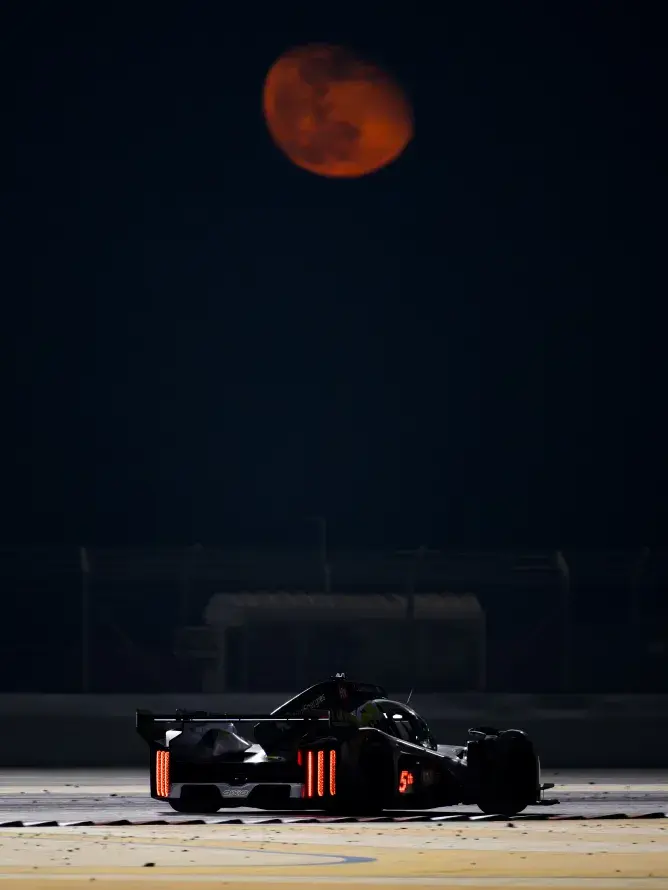 A World Endurance Championship car speeding along the circuit beneath a striking red moon