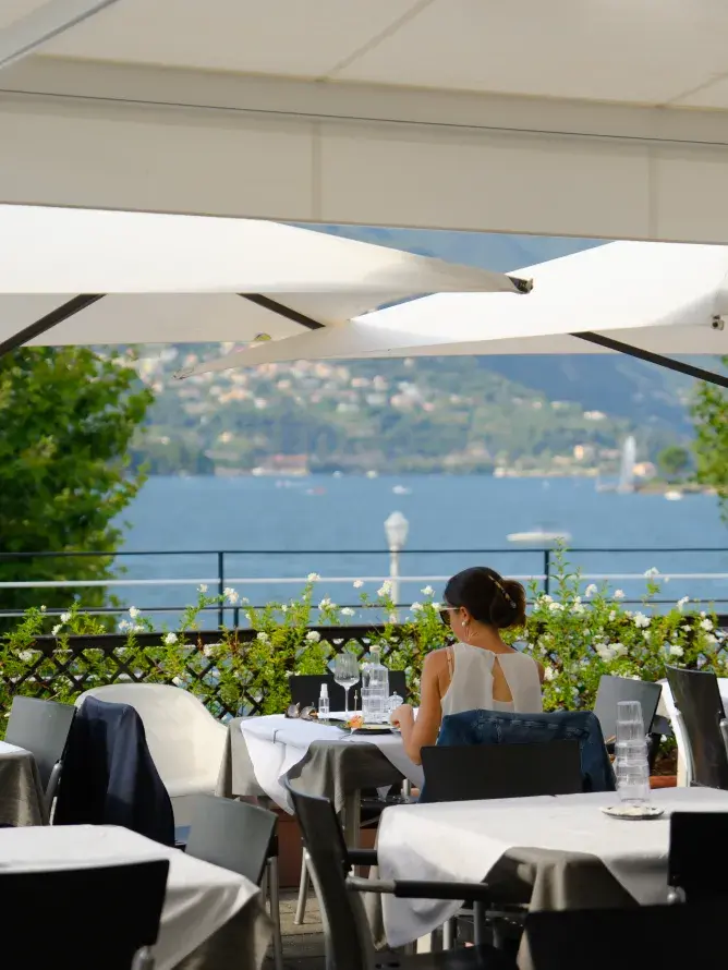 Sunlit lakeside restaurant on Lake Como, with a bright terrace and panoramic view, illustrating the culinary moment included in Sodexo Live! Hospitality’s VIP experience.