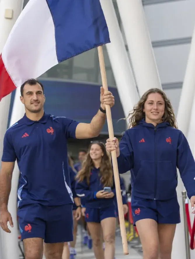 Joueur et joueuse de rugby à 7 de l’équipe de France tenant le drapeau français avant un match à Bordeaux