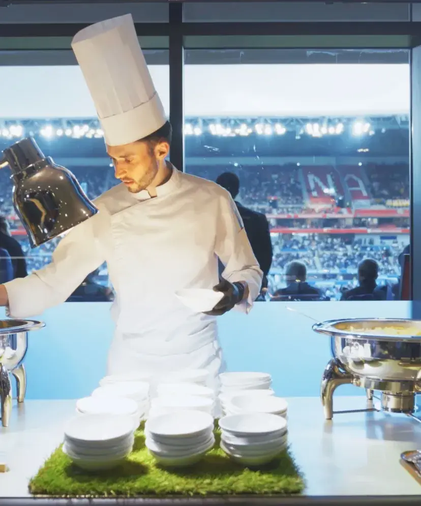 Lenôtre chef in white uniform and toque preparing a gourmet dish in a professional kitchen. He is part of the Sodexo Live! Hospitality VIP services delivered at major sporting events in France and around the world.